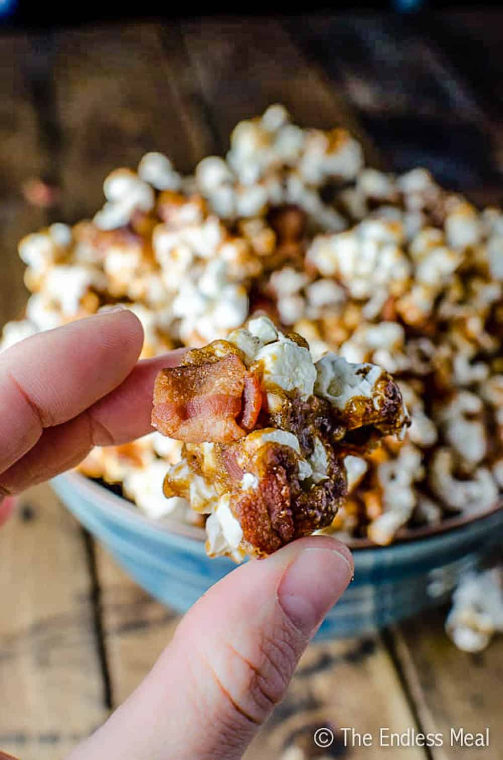A hand holding a cluster of Bourbon Caramel Popcorn with bacon