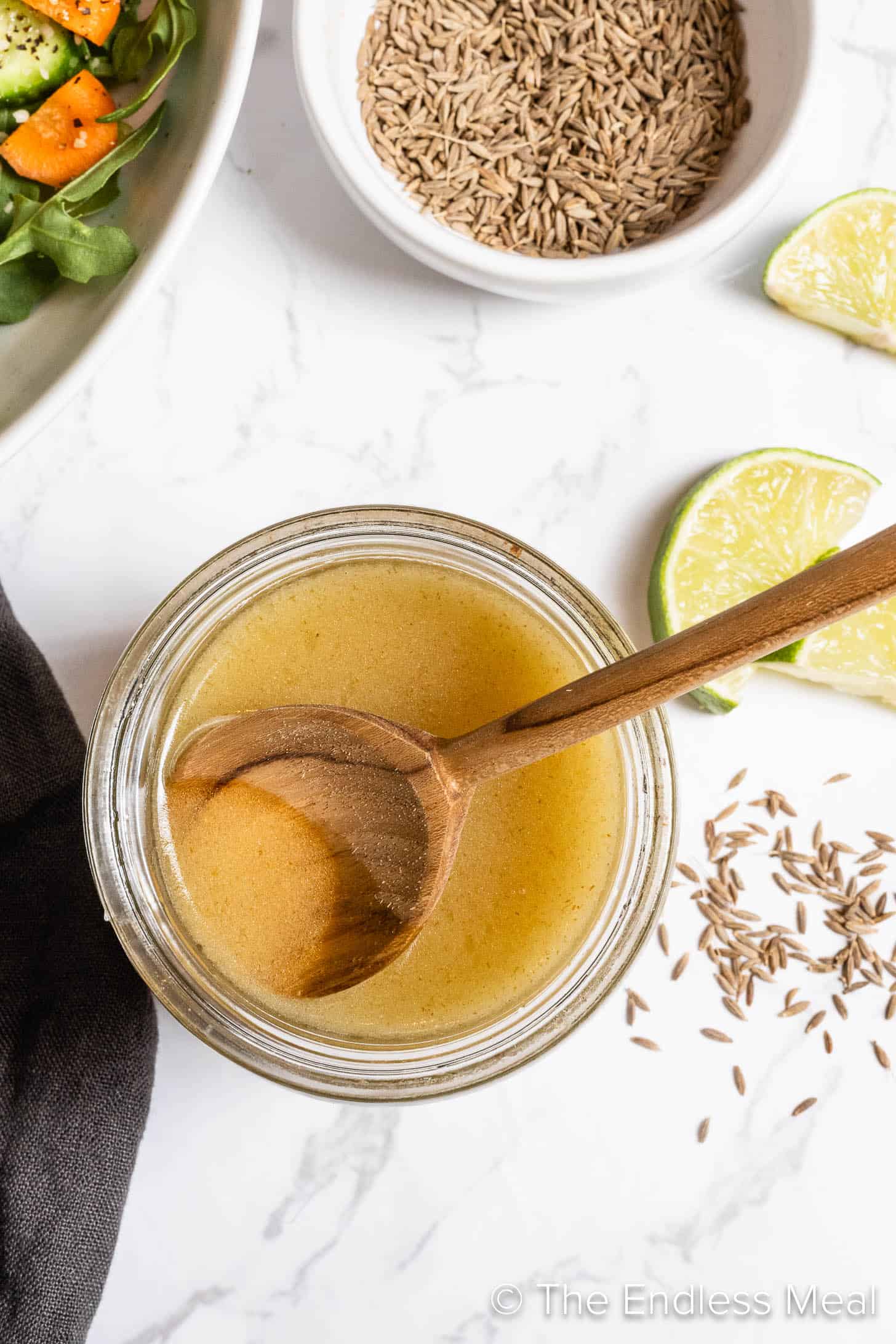 Looking down on lime cumin vinaigrette in a jar with a wooden spoon