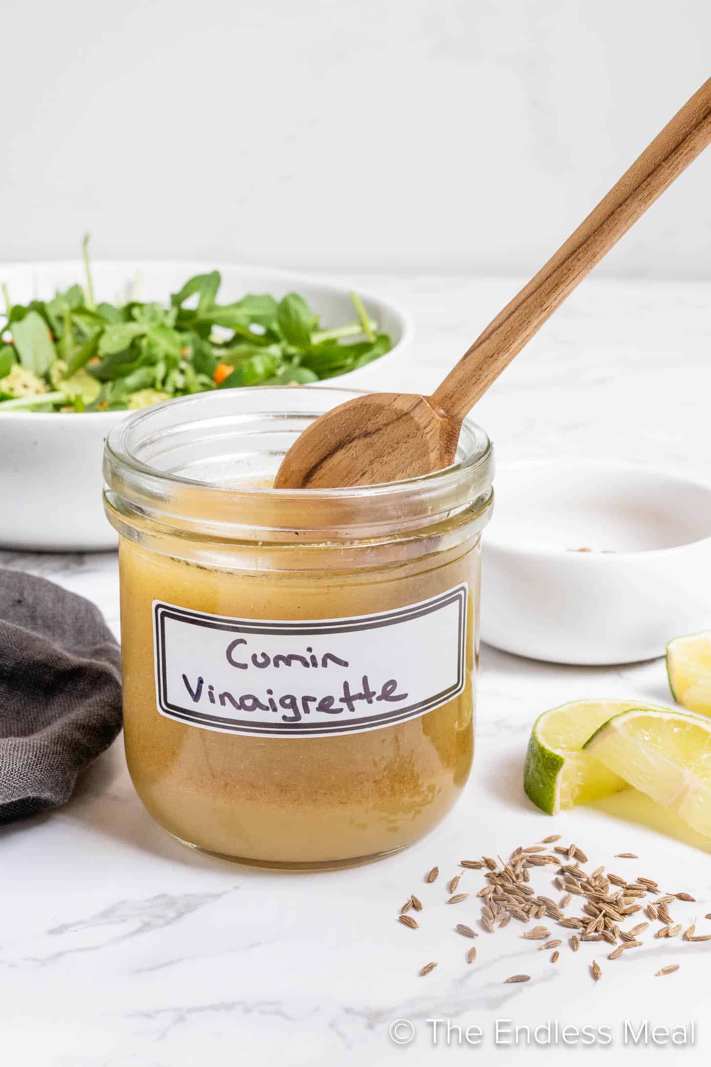 Cumin Lime Vinaigrette in a glass jar with a salad