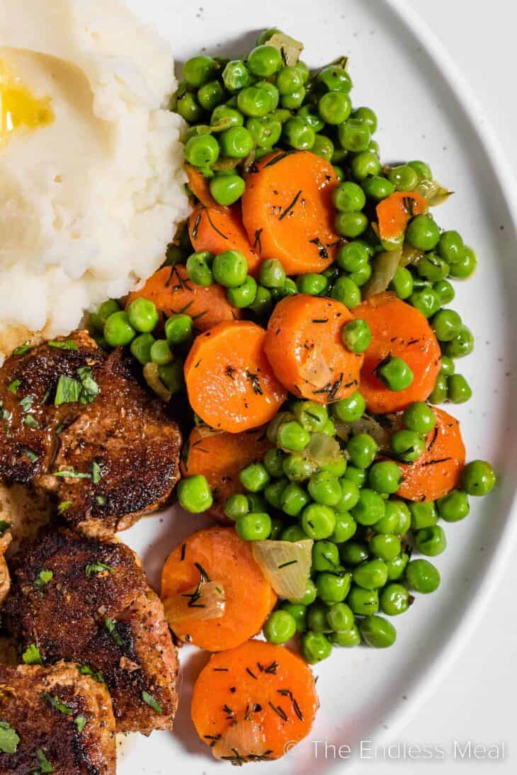 peas and carrots on a dinner plate with mashed potatoes and pork