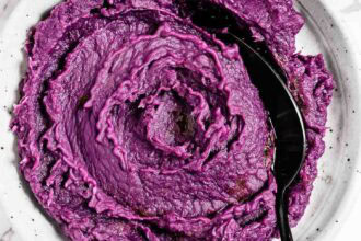 A plate of mashed purple sweet potatoes with a black serving spoon.