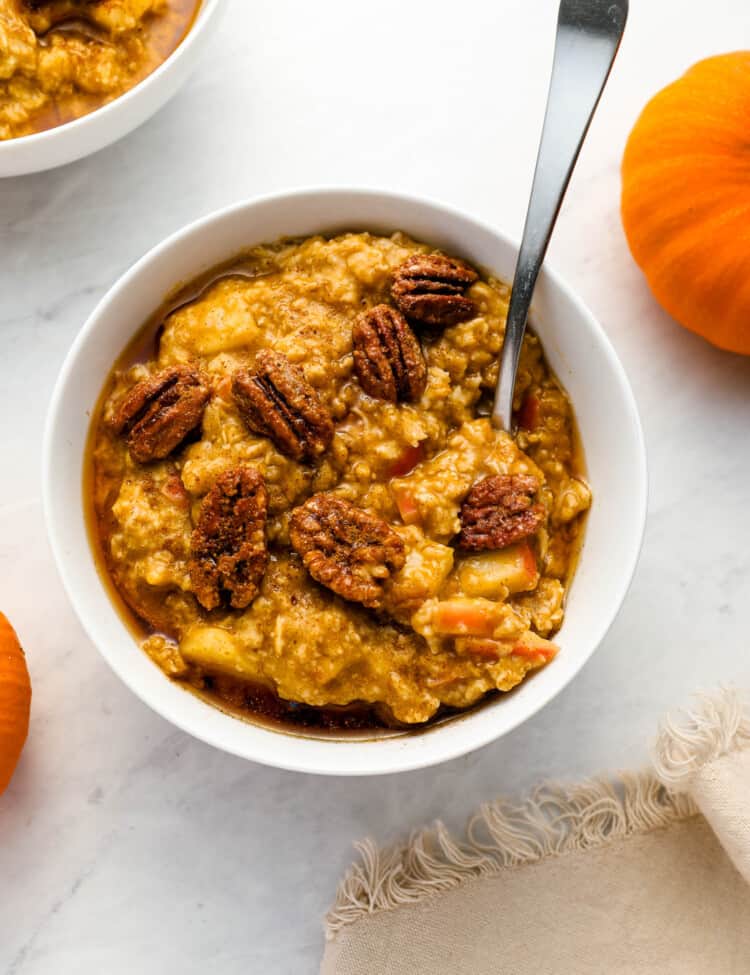 Pumpkin Oatmeal with apples surrounded by pumpkins on a breakfast table.