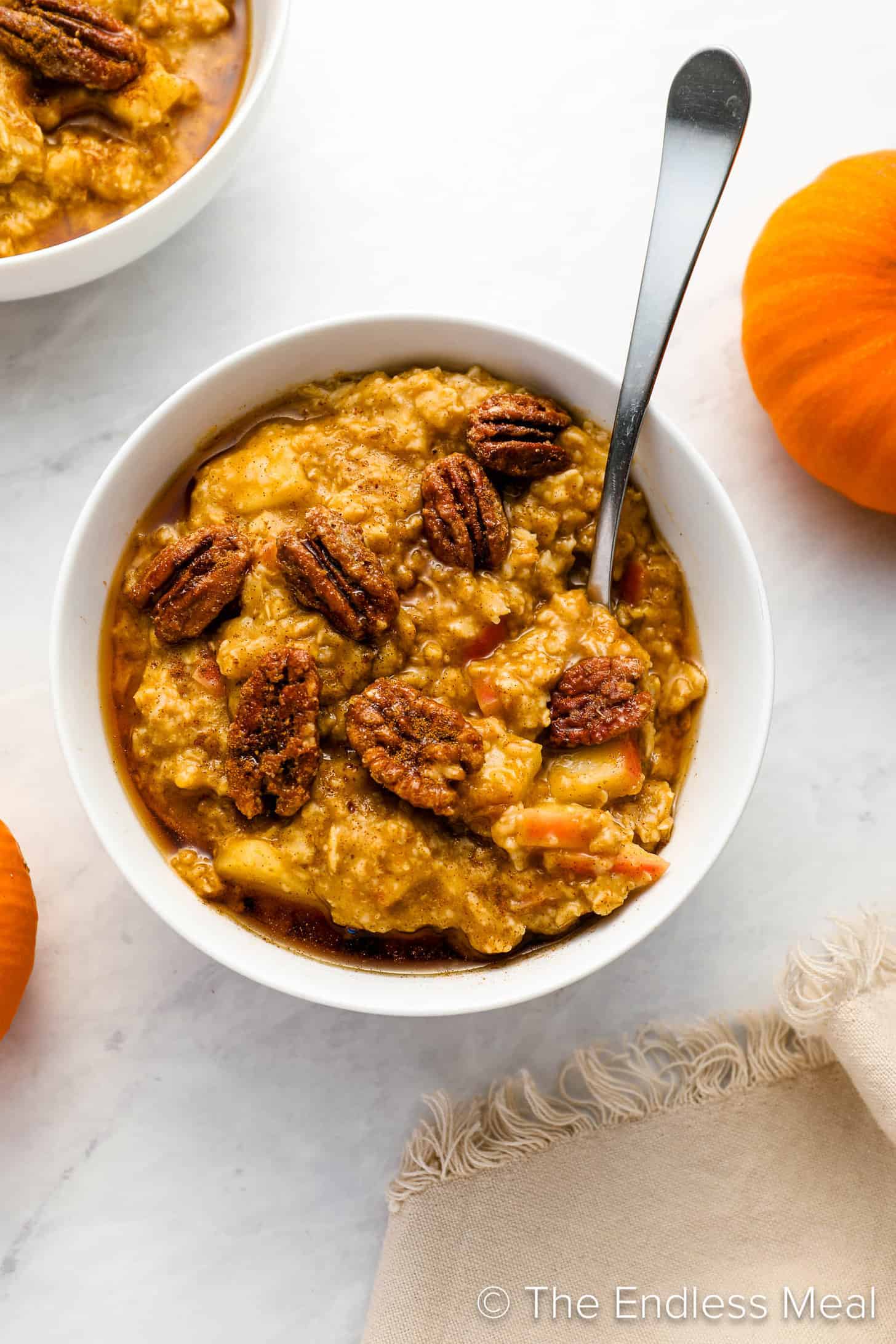 Pumpkin Oatmeal with apples surrounded by pumpkins on a breakfast table.