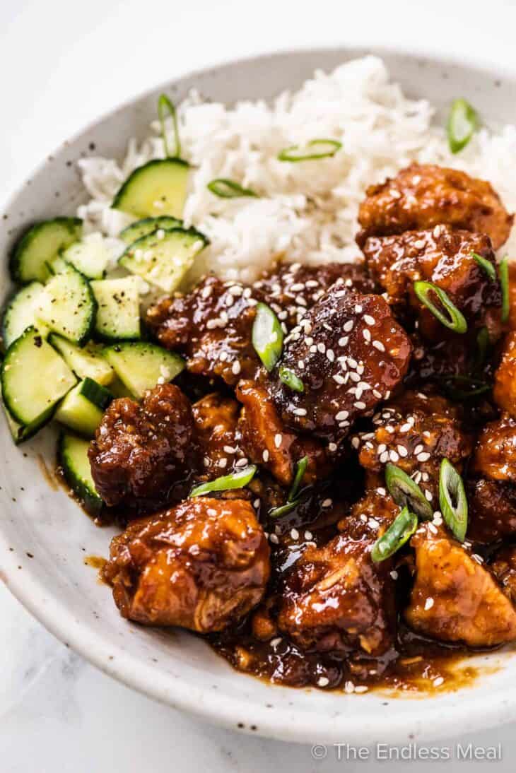 a close up of General Tso's Chicken with rice and cucumber salad