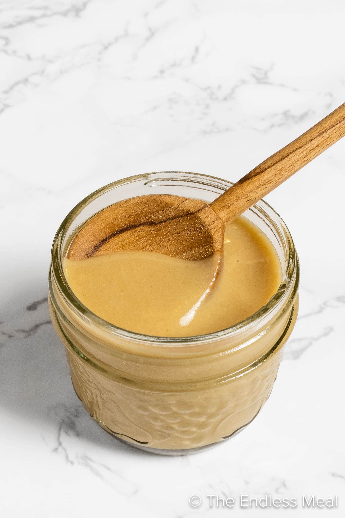 A jar of Maple Tahini Dressing with a spoon