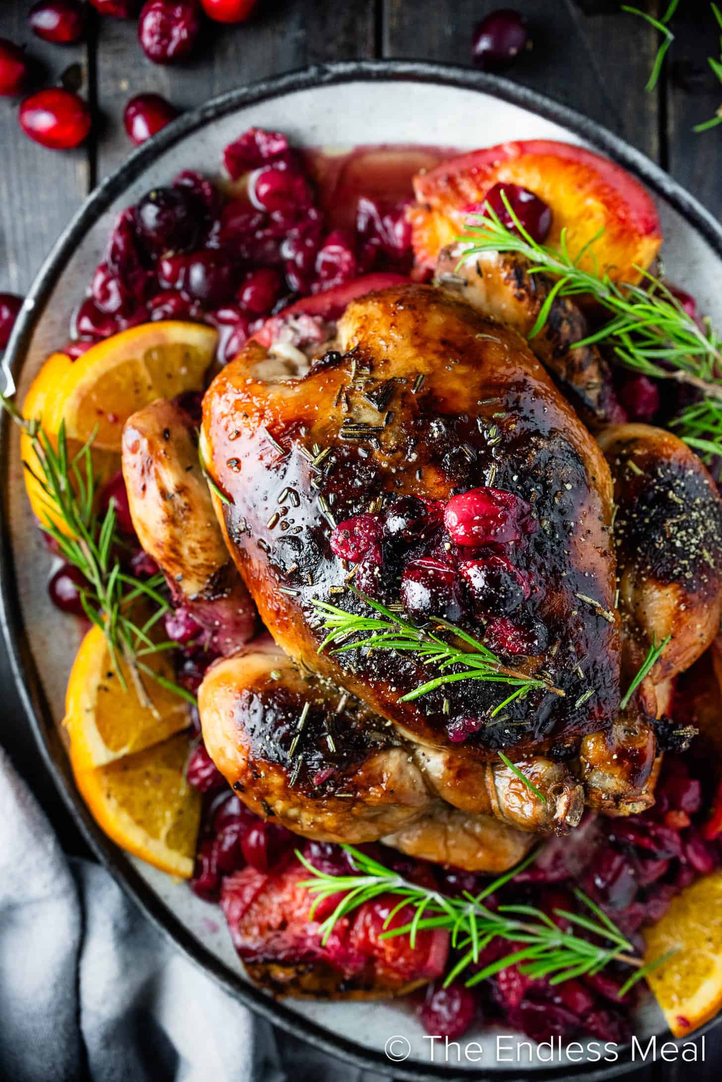 Cranberry Roasted Chicken on a serving platter with oranges and rosemary