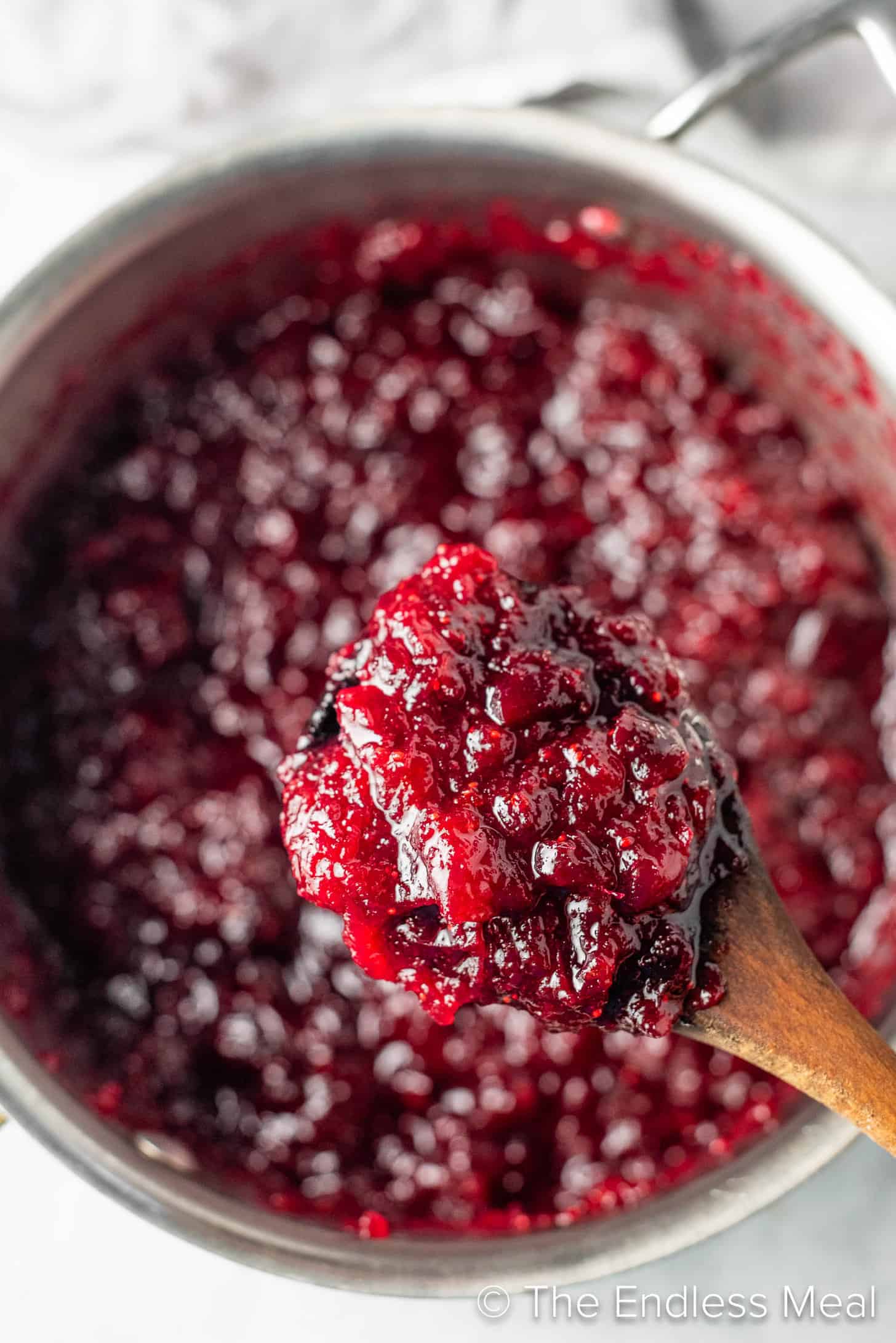 A wooden spoon scooping some Ginger Orange Cranberry Sauce out of a pot