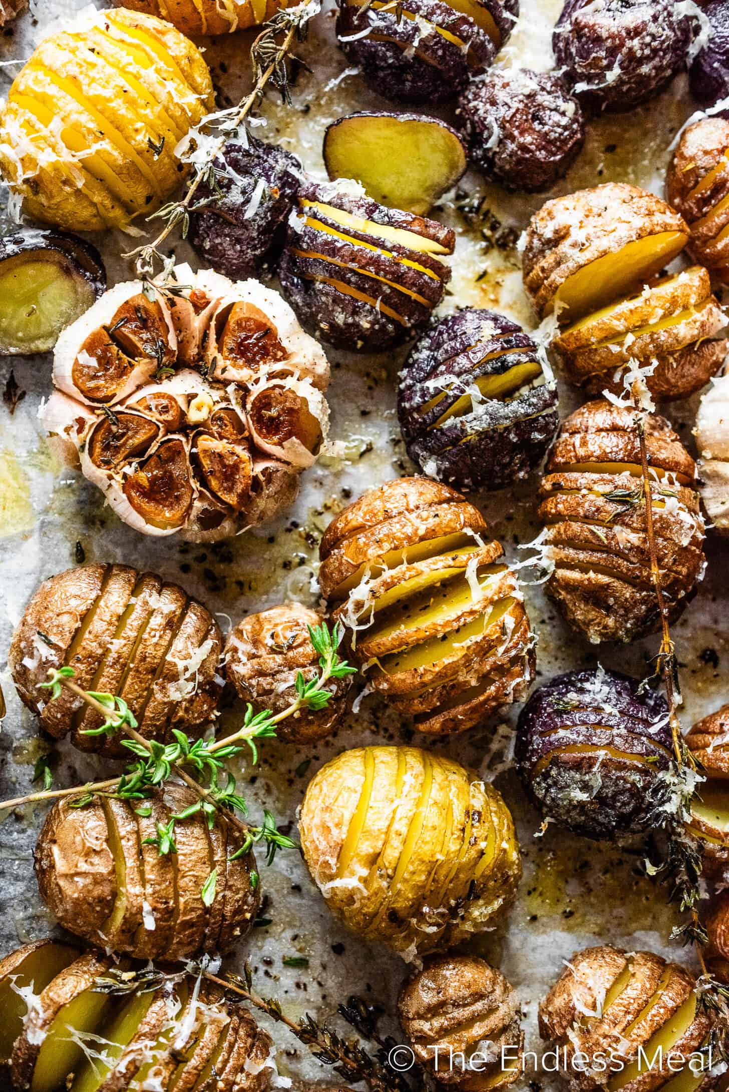 Mini Hasselback Potatoes and roasted garlic on a baking sheet