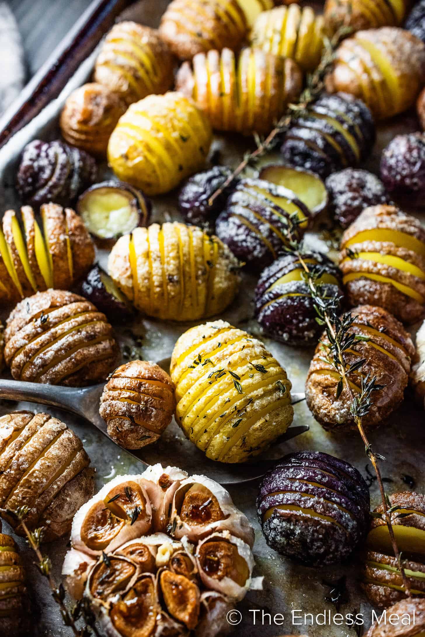 A spoon scooping two Mini Hasselback Potatoes off a baking sheet