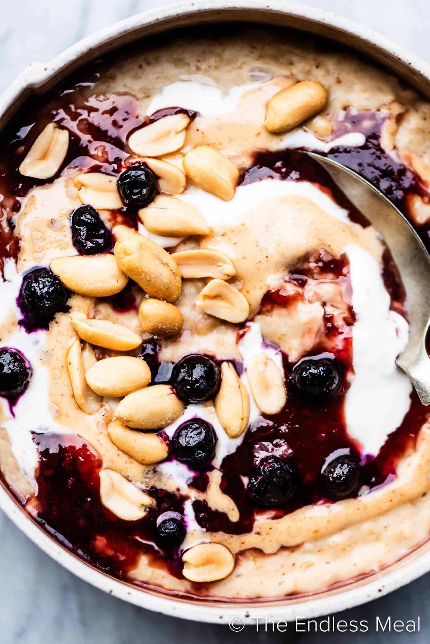 a close up of Peanut Butter Oatmeal in a bowl with jam and blueberries