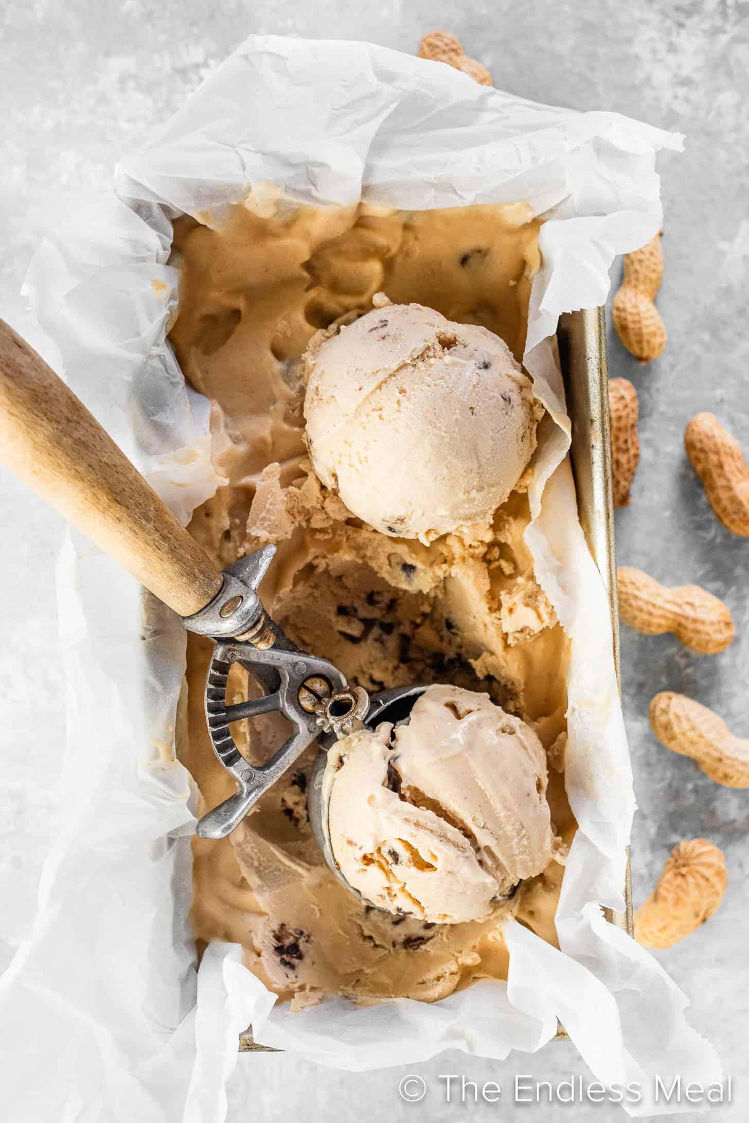 An ice cream scoop scooping out balls of Peanut Butter Cookie Dough Ice Cream from a container.