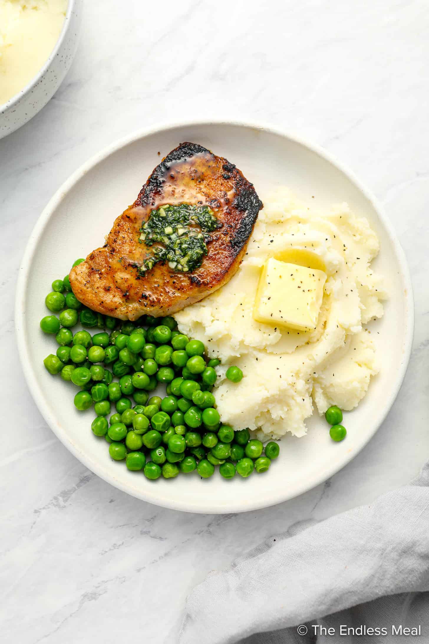 thin pork chops on a dinner plate with mashed potatoes and peas