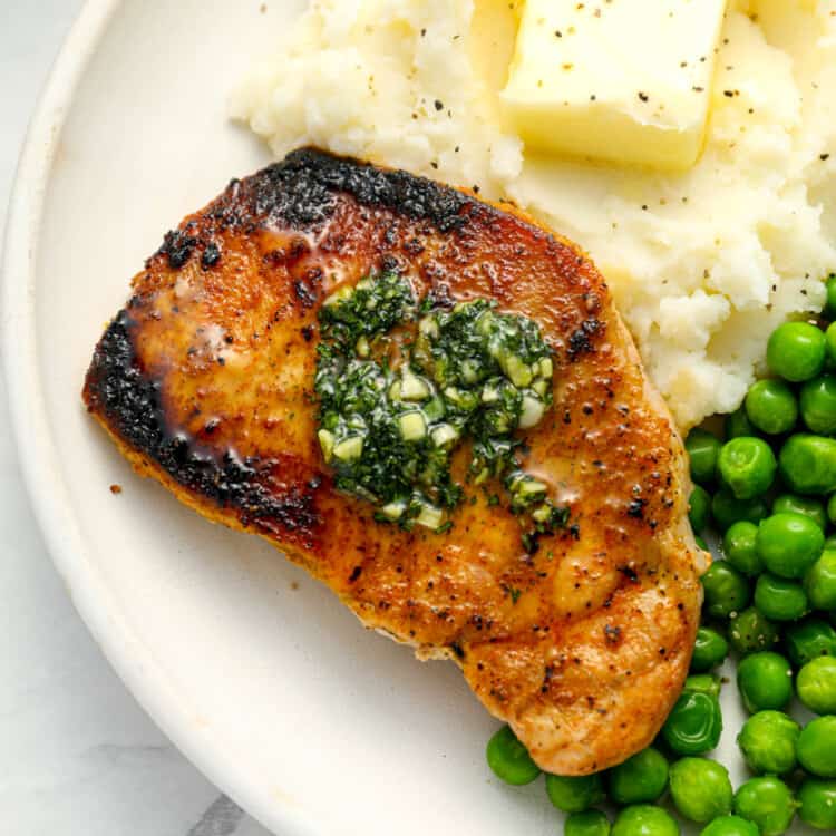 A thin pork chop on a dinner plate with mashed potatoes and peas.