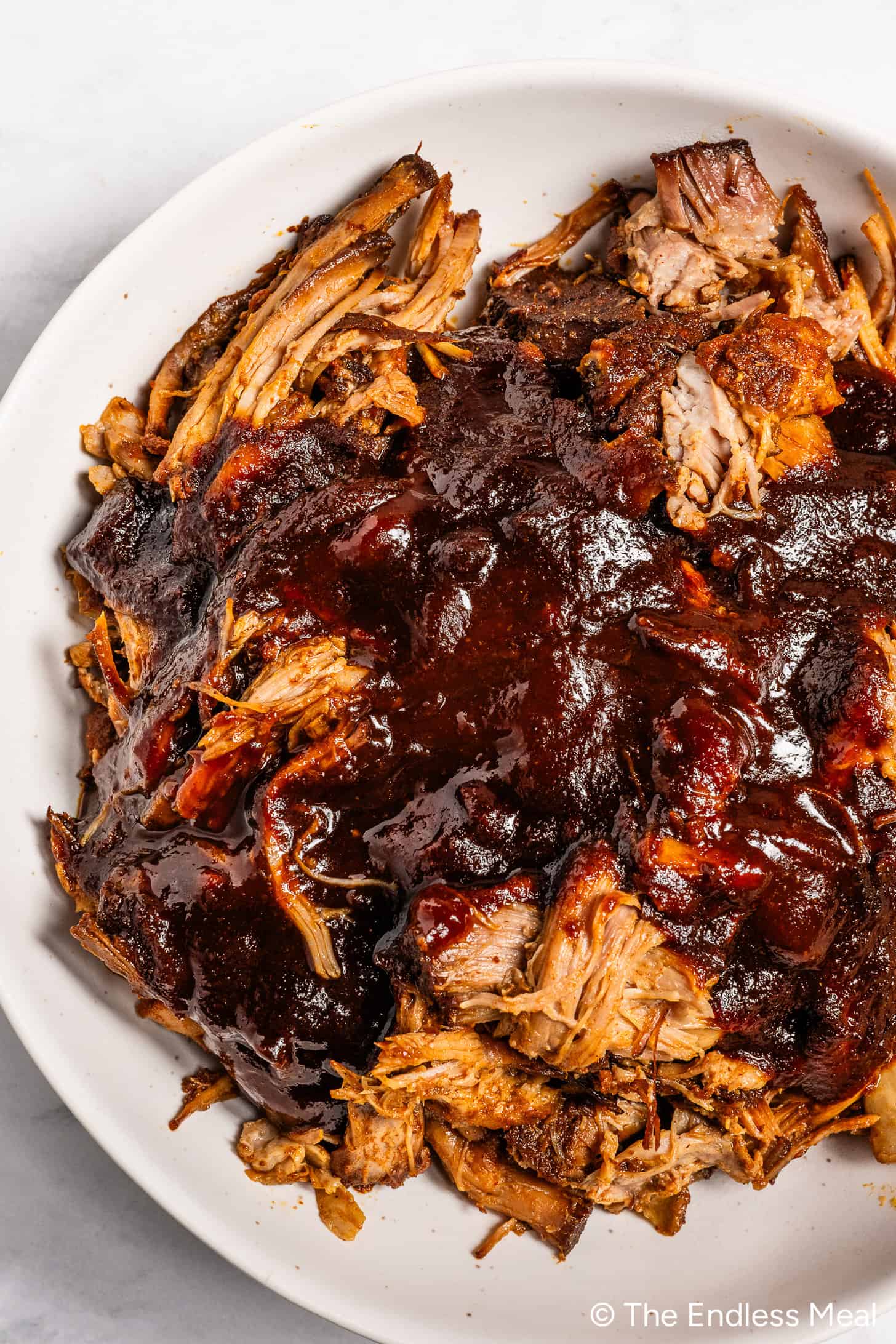 A close up of our favorite BBQ Sauce for Pulled Pork poured over a bowl of pulled pork