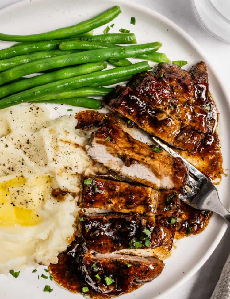 Balsamic Pork Chops sliced on a dinner plate with mashed potatoes and green beans