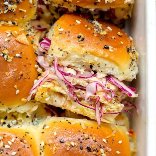 Close-up of golden baked Buffalo Chicken Sliders topped with sesame and poppy seeds, filled with shredded chicken and purple cabbage slaw.