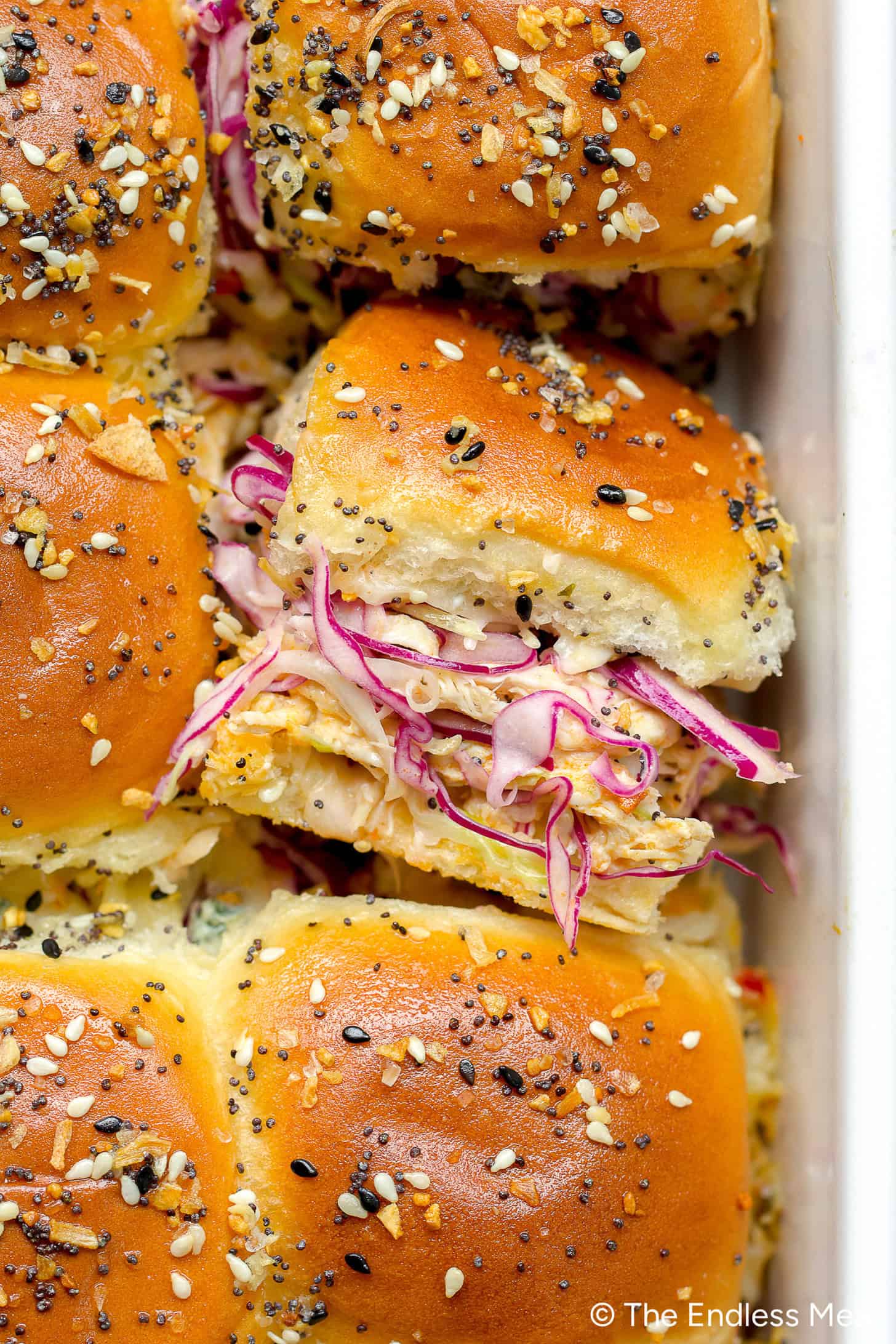 Close-up of golden baked Buffalo Chicken Sliders topped with sesame and poppy seeds, filled with shredded chicken and purple cabbage slaw.