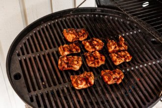 Several pieces of grilled BBQ chicken are sizzling on a round barbecue grill, with dark char marks visible on the surface.