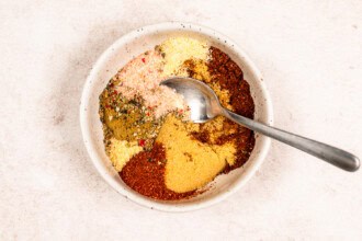 A bowl containing various colorful spices arranged in sections with a metal spoon resting inside, perfect for seasoning Grilled BBQ Chicken.