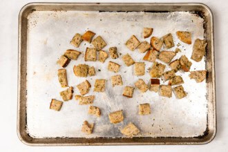image for recipe instruction: A baking sheet with scattered baked croutons on a white background, perfect for topping a fresh Kale and Asparagus Caesar Salad.