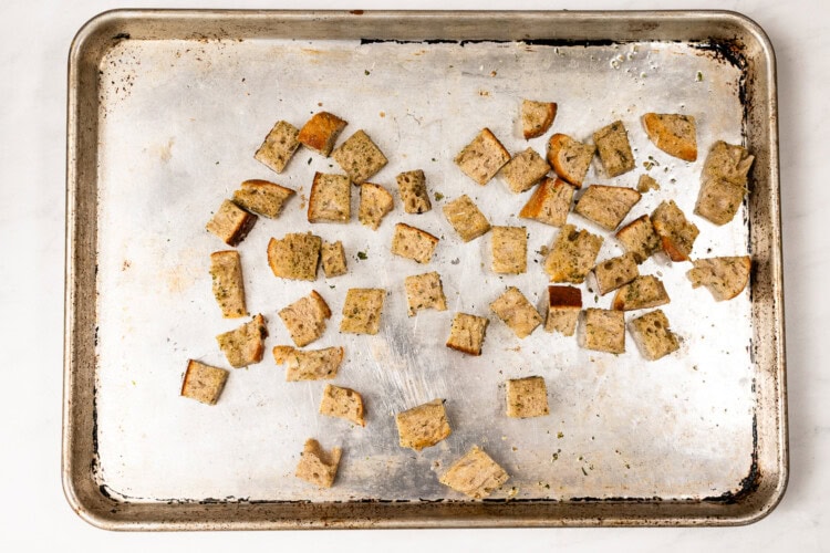 image for recipe instruction: A baking sheet with scattered baked croutons on a white background, perfect for topping a fresh Kale and Asparagus Caesar Salad.