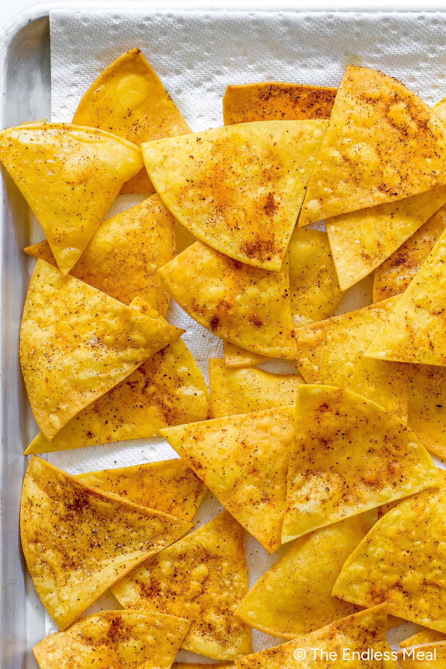 Homemade Tortilla Chips are baked corn tortilla chips with seasoning, spread on a paper towel-lined tray.