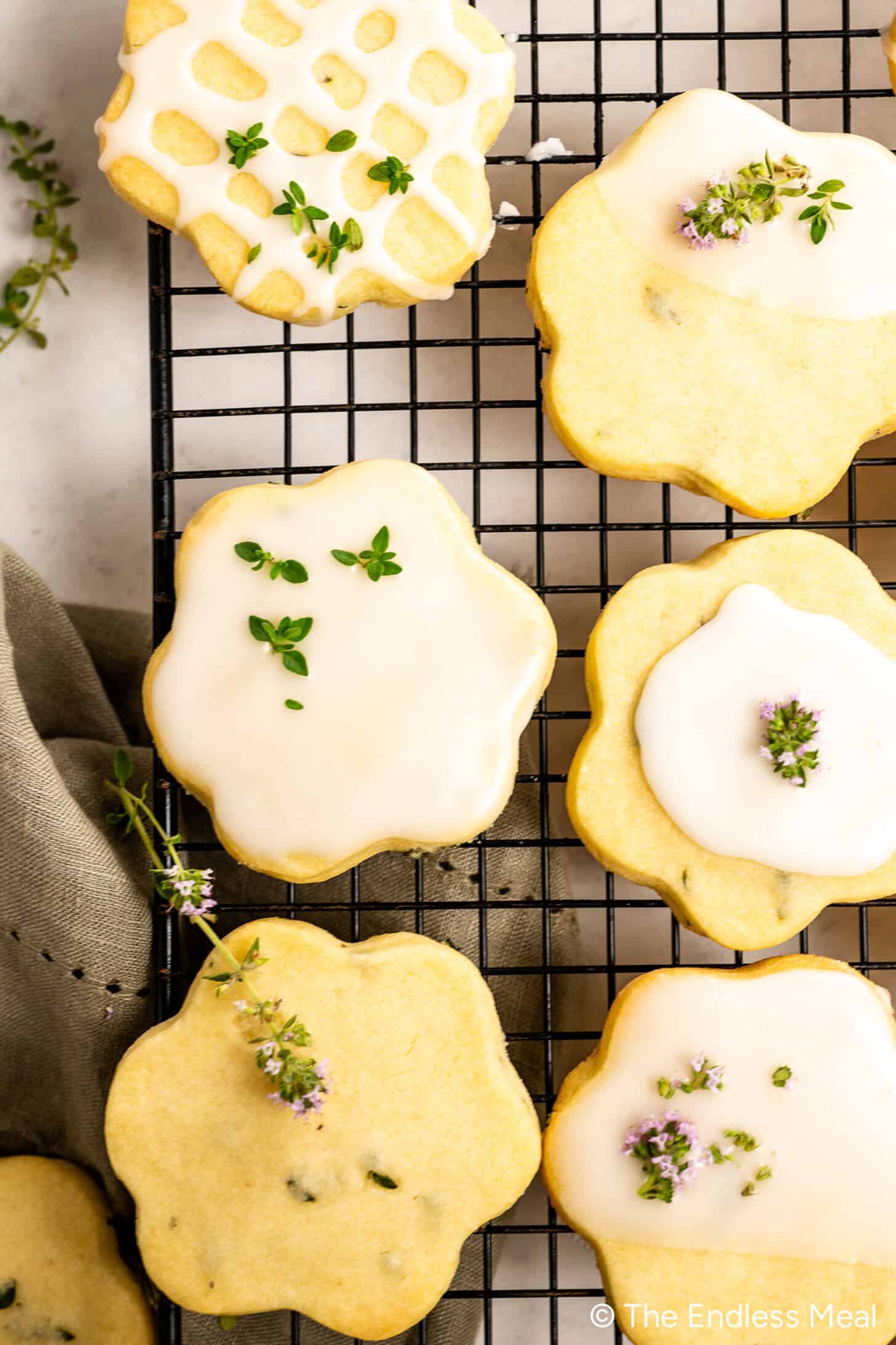 Lemon Thyme Cookies with white glaze and small herb garnishes are arranged on a black wire cooling rack.