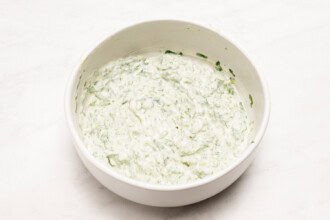 A white bowl filled with creamy, green cilantro mayo sits on a white surface, perfect as a dip or sauce for your favorite fried chicken sandwich.