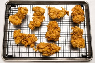 Eight pieces of golden-brown Gochujang Fried Chicken rest on a wire rack placed over a baking sheet after their first fry.