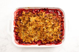 A baked Strawberry Rhubarb Crisp with a golden brown oat topping in a white rectangular dish, filled with vibrant red fruit filling, photographed from above.