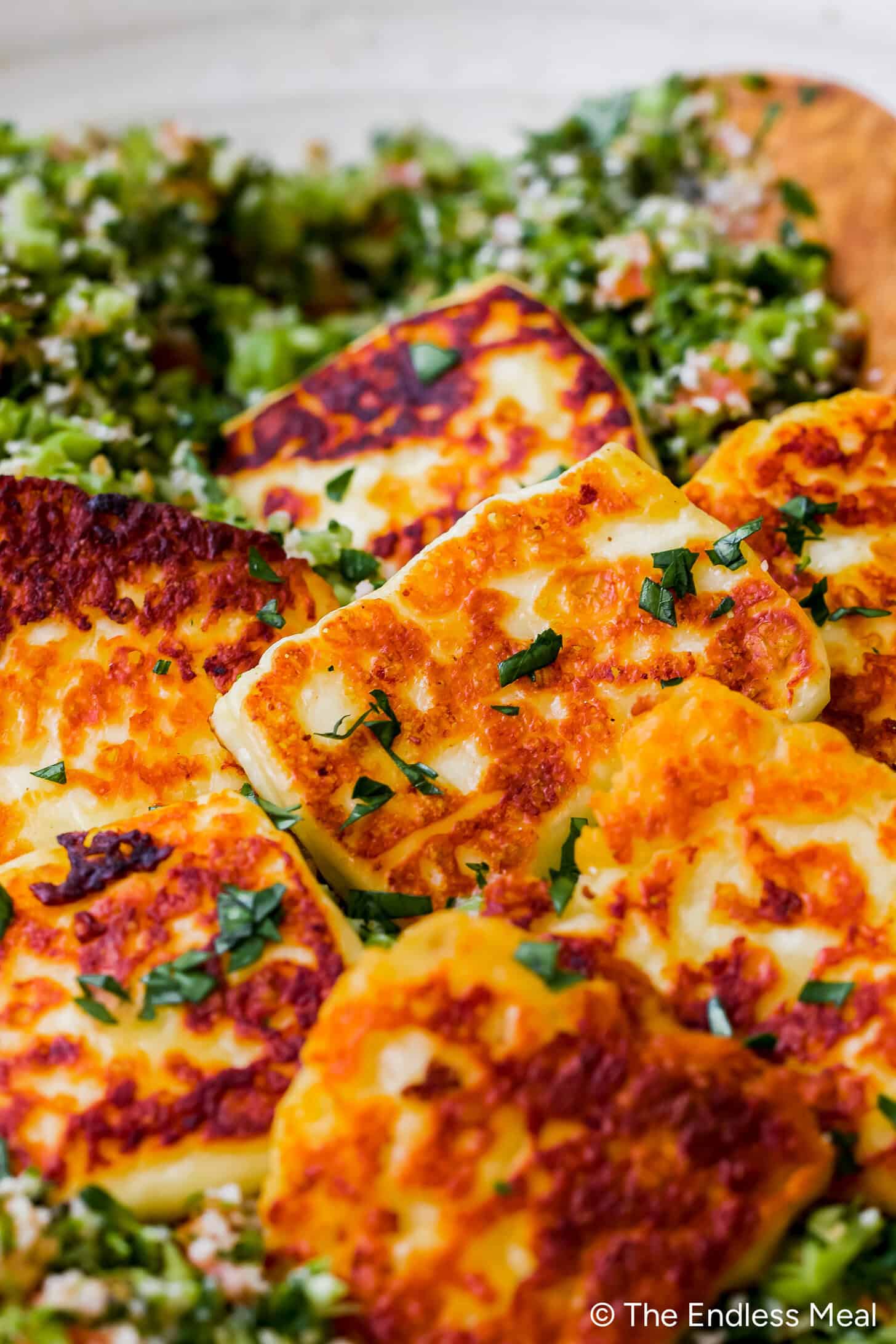 Golden, pan-seared fried halloumi slices topped with chopped herbs, served on a vibrant bed of broccoli tabbouleh for a fresh twist on the classic tabbouleh recipe.