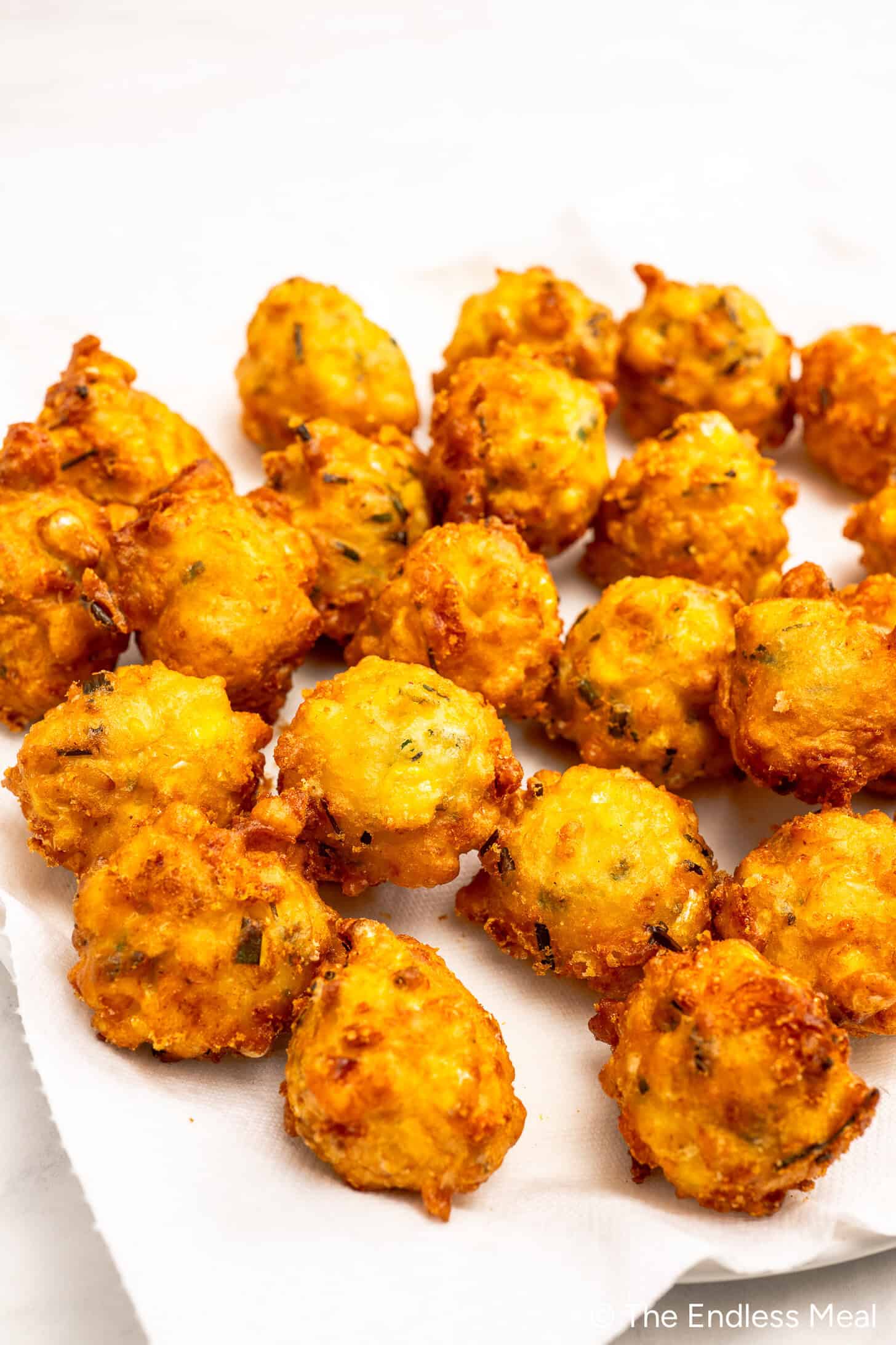A group of golden-brown hush puppies rests on a white paper towel, showing a crispy fried exterior with visible herbs—a classic Southern corn fritters recipe perfect for those who love delicious corn recipes.