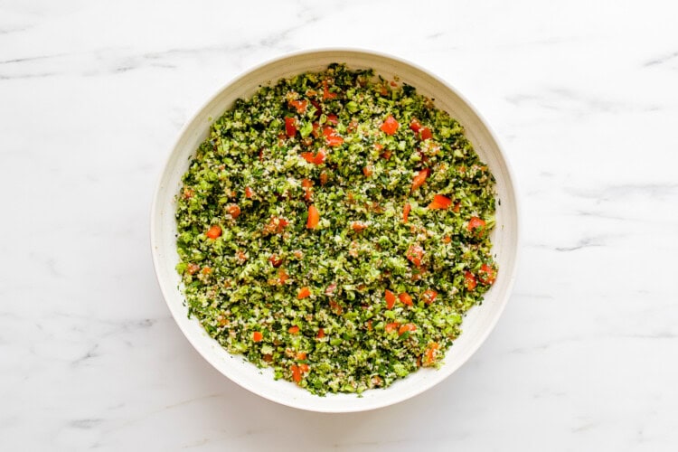 A white bowl filled with tabbouleh salad made of chopped parsley, tomatoes, and bulgur, placed on a white marble surface—perfect alongside crispy fried halloumi.