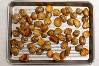 Image for recipe instruction: Roasted halved baby potatoes spread evenly on a metal baking sheet, showing golden brown and crispy edges—perfect as a side for Lemon Butter Salmon.