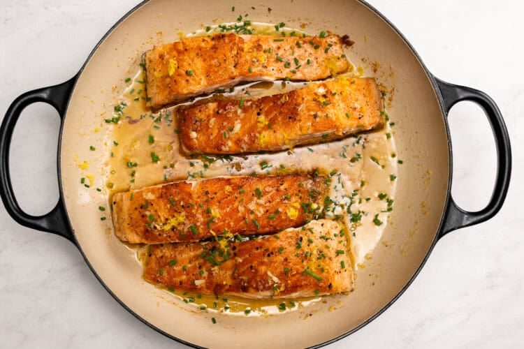 Four cooked salmon fillets are arranged in a round pan with a creamy sauce and garnished with fresh chives—a delightful Lemon Butter Salmon recipe perfect for any dinner table.