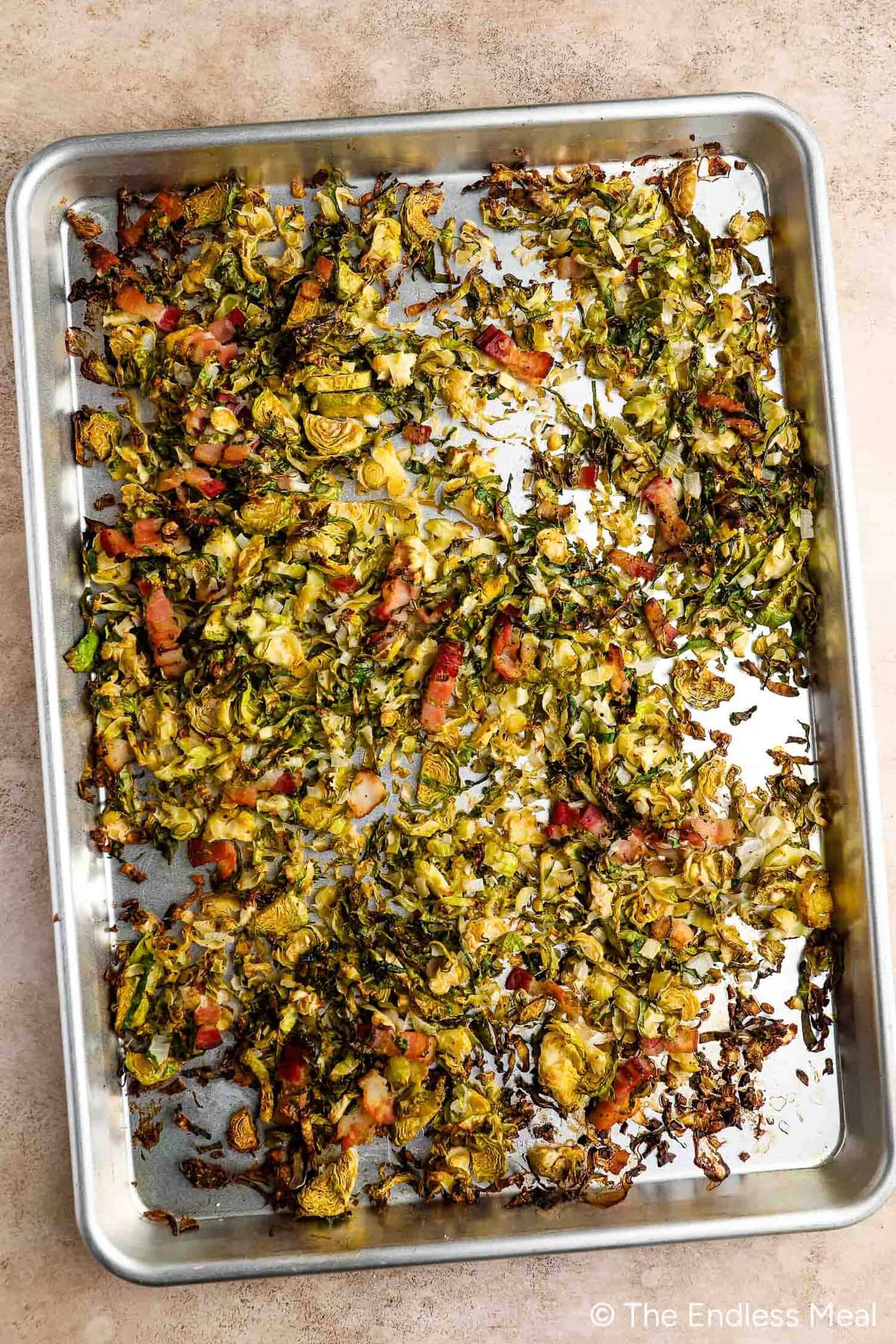 A baking sheet with Roasted Brussels Sprouts and crispy pieces of bacon scattered across it.