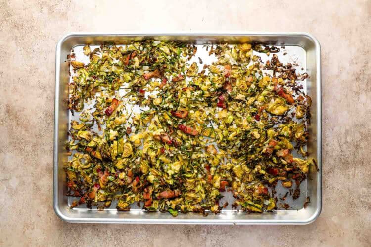 A baking sheet with thinly sliced roasted Brussels sprouts and pieces of bacon on a light-colored surface, perfect as a savory side or tossed into your favorite pasta dish.