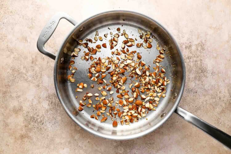 A stainless steel skillet with chopped almonds being toasted on a light-colored countertop, perfect for adding crunch to roasted Brussels sprouts or pasta dishes.
