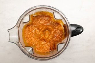 Blender filled with smooth orange Pumpkin Tomato Soup puree, viewed from above, placed on a light-colored countertop.