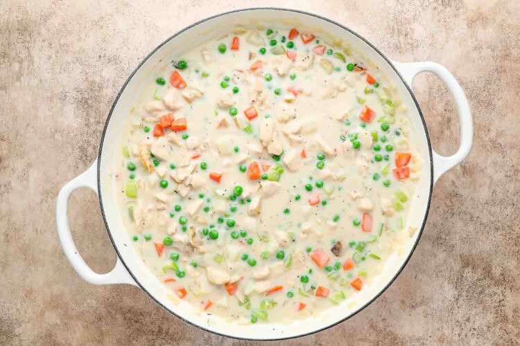 A white pot filled with creamy Chicken Pot Pie with Biscuits mixture, brimming with tender chicken, peas, carrots, and celery.