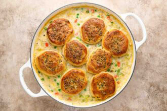 A white casserole dish filled with creamy Chicken Pot Pie with Biscuits, featuring eight golden-brown biscuits atop a mix of tender chicken and vegetables.