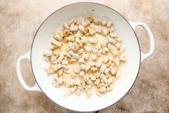 Diced pieces of cooked chicken breast in a white pan on a beige textured surface, perfect for making Chicken Pot Pie with Biscuits.