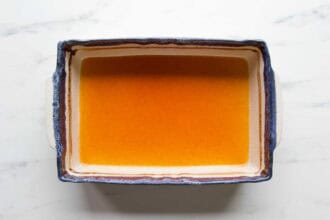 A rectangular baking dish filled with an orange liquid, perfect for making Chicken Veggie Enchiladas, sits on a white marble surface.