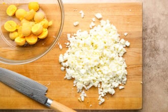 Chopped egg whites on a wooden cutting board, whole egg yolks in a glass bowl, and a knife beside them.