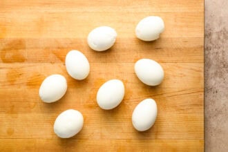 Seven peeled hard-boiled eggs are arranged on a wooden cutting board.