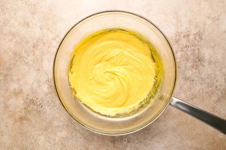 A glass mixing bowl with yellow cake batter swirled in the center sits on a light, textured countertop, reminiscent of the rich, creamy texture found in Homemade Hollandaise Sauce for Classic Eggs Benedict.
