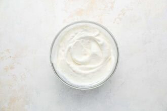 A glass bowl filled with plain, creamy yogurt sits on a light-colored surface, ready to complement your Holiday Brussels Sprouts.