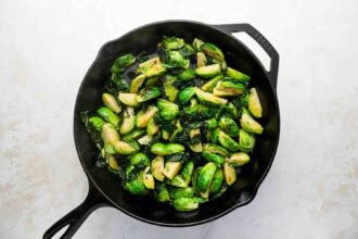Holiday Brussels Sprouts being sautéed in a black cast iron skillet on a light-colored countertop.