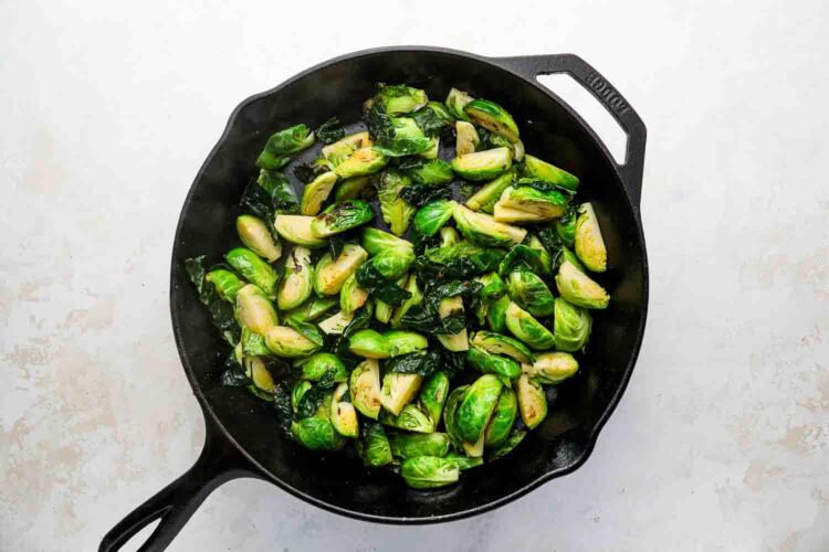 Holiday Brussels Sprouts being sautéed in a black cast iron skillet on a light-colored countertop.