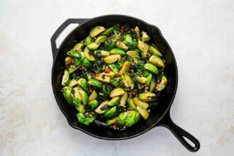 Sliced Brussels sprouts sautéed with herbs and spices in a black cast iron skillet, set on a light-colored surface.